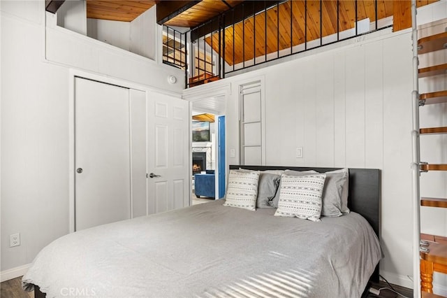 bedroom with a closet, baseboards, lofted ceiling with beams, wood ceiling, and a lit fireplace