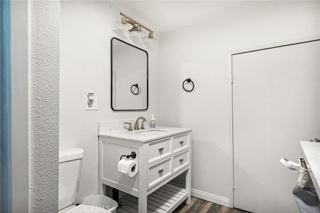bathroom with toilet, wood finished floors, vanity, and baseboards
