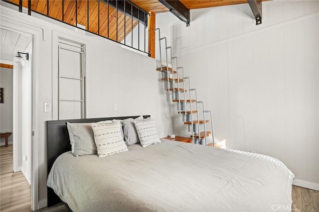 bedroom with beam ceiling, wood walls, and wood-type flooring