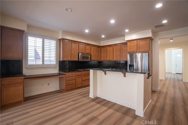 kitchen with stainless steel appliances, light hardwood / wood-style flooring, backsplash, a breakfast bar area, and built in desk