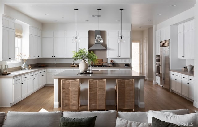 kitchen featuring white cabinetry, wall chimney exhaust hood, decorative light fixtures, and a center island