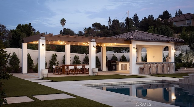 back house at dusk with a yard, exterior bar, a patio, and a fenced in pool