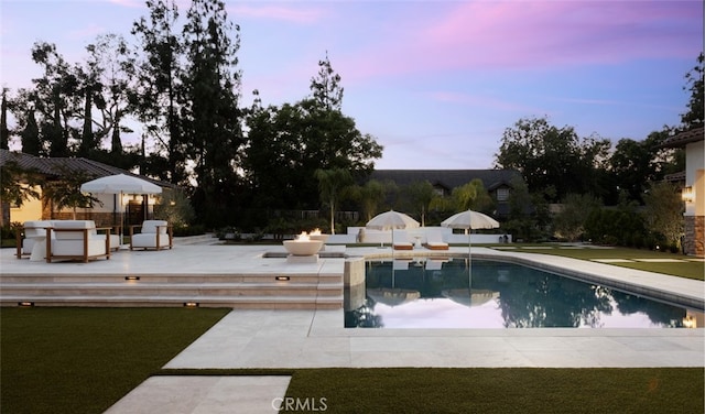 pool at dusk with a patio area and a lawn