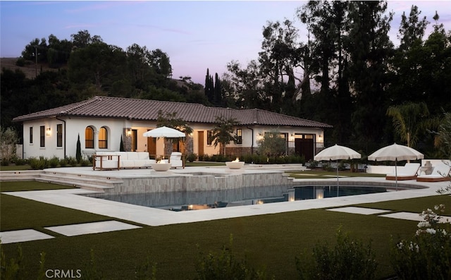 back house at dusk with a patio area and a lawn