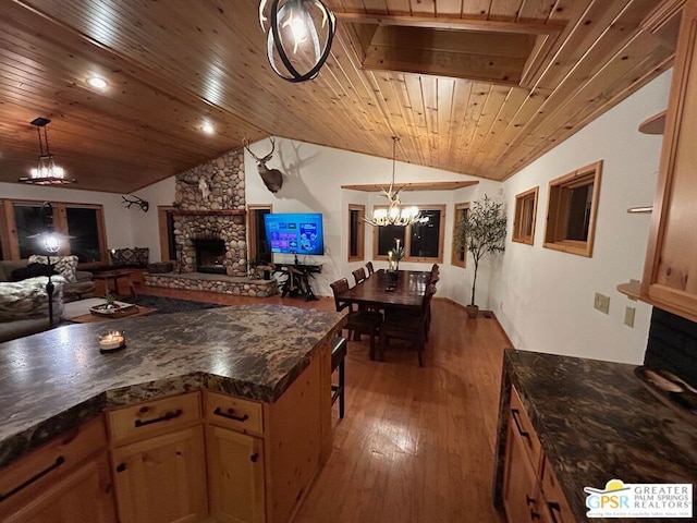 kitchen featuring vaulted ceiling, a stone fireplace, pendant lighting, and light hardwood / wood-style floors