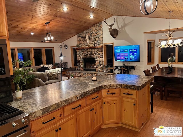 kitchen featuring lofted ceiling, light hardwood / wood-style flooring, a stone fireplace, a notable chandelier, and decorative light fixtures