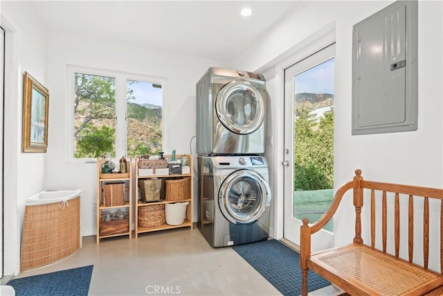 laundry area featuring electric panel, stacked washer and dryer, and a wealth of natural light