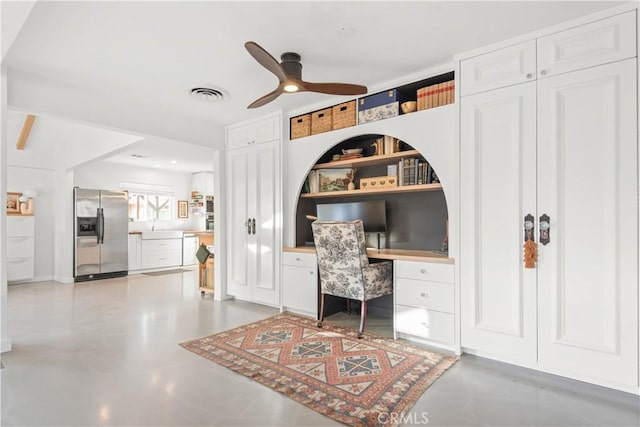 office space featuring ceiling fan, built in desk, sink, and concrete flooring