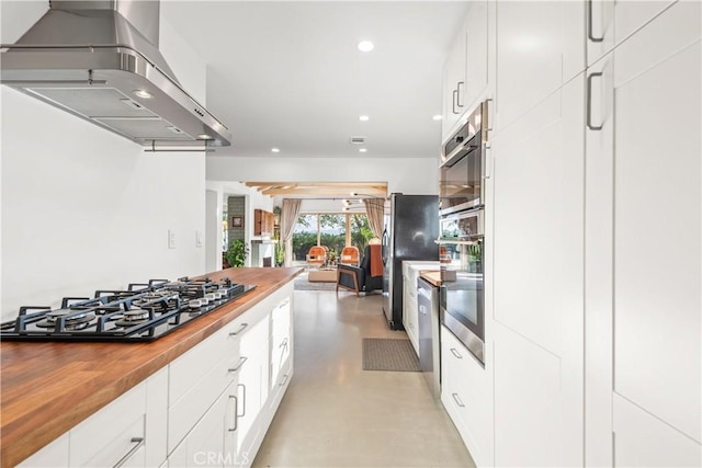 kitchen with stainless steel appliances, white cabinetry, wooden counters, and wall chimney range hood