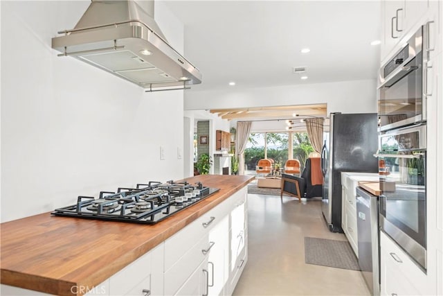 kitchen with butcher block countertops, island range hood, white cabinetry, and appliances with stainless steel finishes