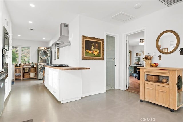 kitchen with wall oven, stacked washer and dryer, white cabinets, and range hood