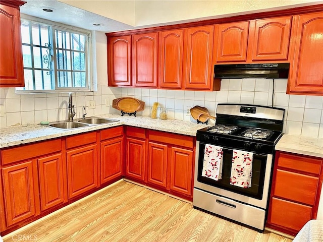 kitchen with backsplash, sink, stainless steel gas stove, light stone countertops, and light wood-type flooring