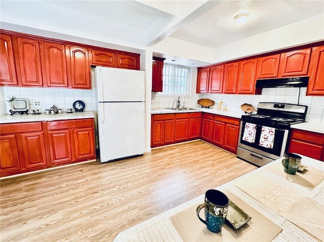 kitchen with white refrigerator, sink, stainless steel stove, light wood-type flooring, and tasteful backsplash