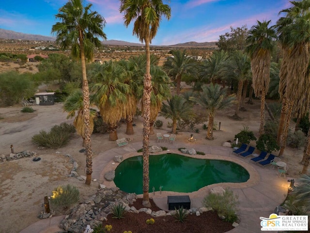 pool at dusk featuring a mountain view and a patio