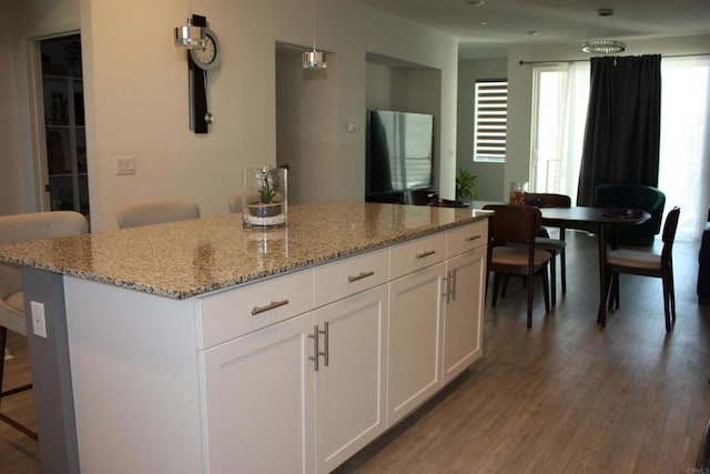 kitchen with white cabinetry, light stone countertops, hanging light fixtures, a breakfast bar area, and a kitchen island