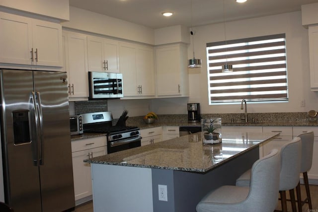 kitchen featuring stainless steel appliances, a kitchen island, dark stone counters, decorative light fixtures, and white cabinets