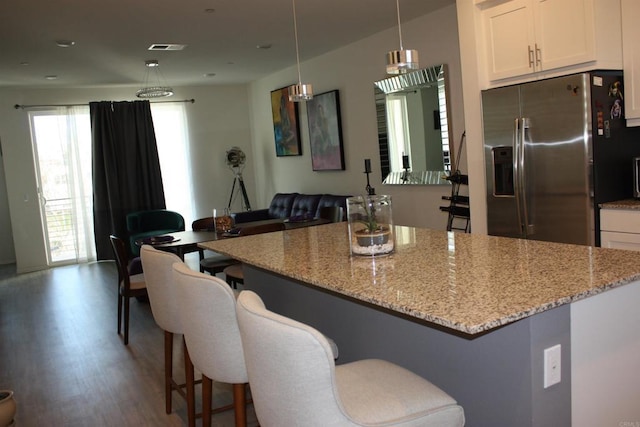 kitchen featuring stainless steel fridge, wood-type flooring, white cabinetry, and hanging light fixtures