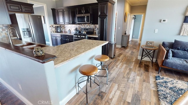 kitchen with decorative backsplash, dark brown cabinets, appliances with stainless steel finishes, a kitchen breakfast bar, and light hardwood / wood-style floors