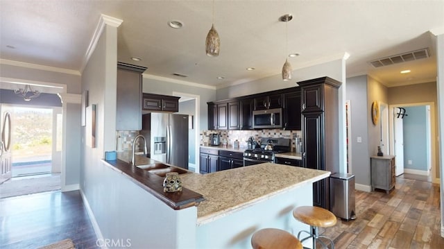 kitchen with dark wood-type flooring, kitchen peninsula, stainless steel appliances, light stone countertops, and decorative light fixtures