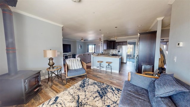 living room featuring crown molding, wood-type flooring, a wood stove, and ceiling fan