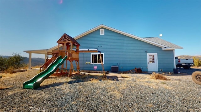 rear view of house with central AC and a playground