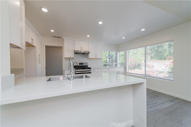 kitchen featuring white cabinetry, a sink, under cabinet range hood, stainless steel range with gas stovetop, and recessed lighting