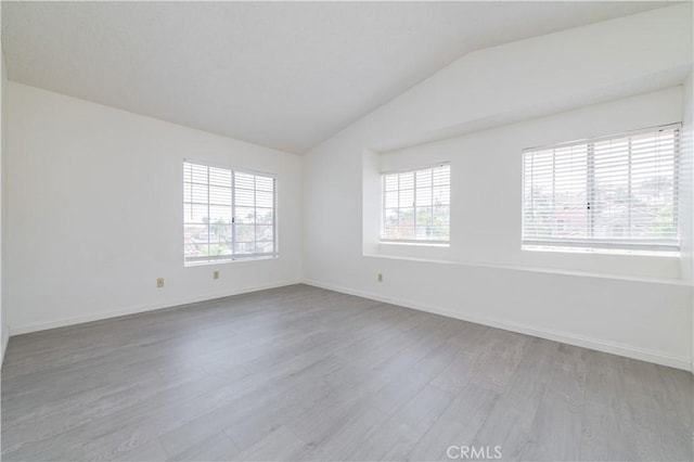 empty room with vaulted ceiling, wood finished floors, and plenty of natural light