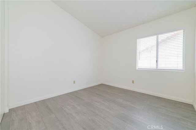unfurnished room with lofted ceiling, light wood-style floors, and baseboards
