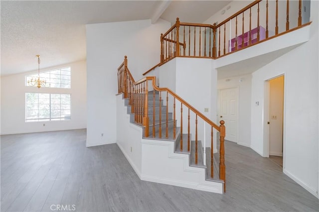 stairway with beam ceiling, a chandelier, high vaulted ceiling, baseboards, and wood finished floors