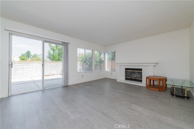 unfurnished living room featuring a textured ceiling, wood finished floors, and a brick fireplace