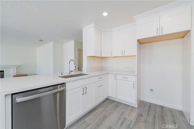 kitchen featuring light countertops, stainless steel dishwasher, a peninsula, and a sink
