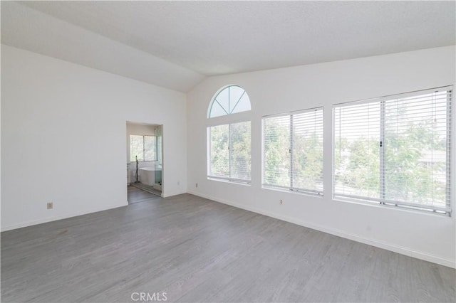 empty room featuring vaulted ceiling, wood finished floors, and baseboards