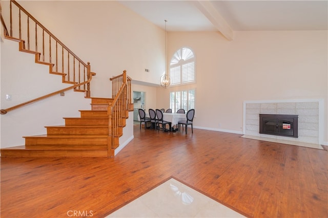 unfurnished living room with beam ceiling, hardwood / wood-style flooring, high vaulted ceiling, and a chandelier