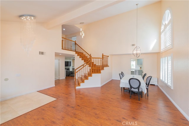 unfurnished dining area featuring high vaulted ceiling, beamed ceiling, an inviting chandelier, and hardwood / wood-style floors