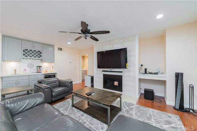 living room featuring beverage cooler, ceiling fan, a fireplace, light hardwood / wood-style floors, and wet bar