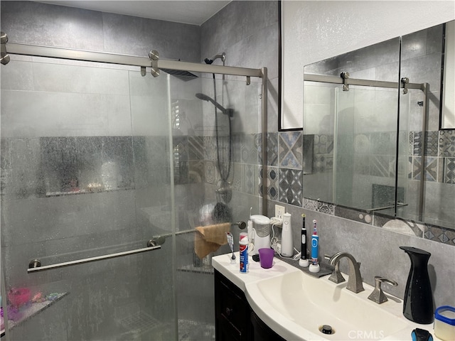 bathroom with vanity, decorative backsplash, a shower with shower door, and tile walls