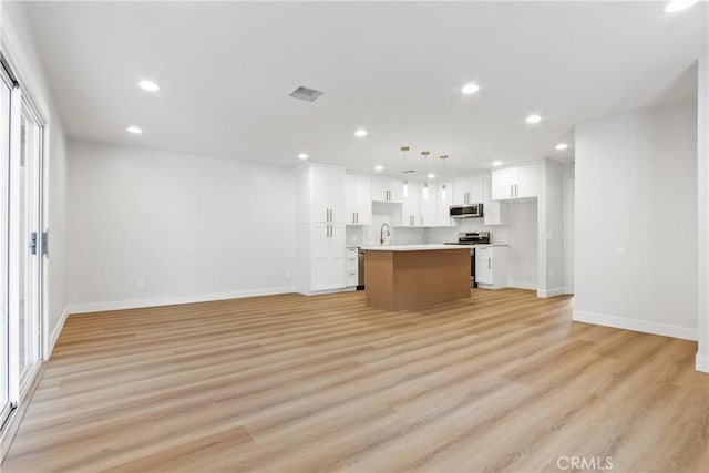 kitchen with a kitchen island, white cabinetry, stainless steel appliances, light hardwood / wood-style floors, and hanging light fixtures