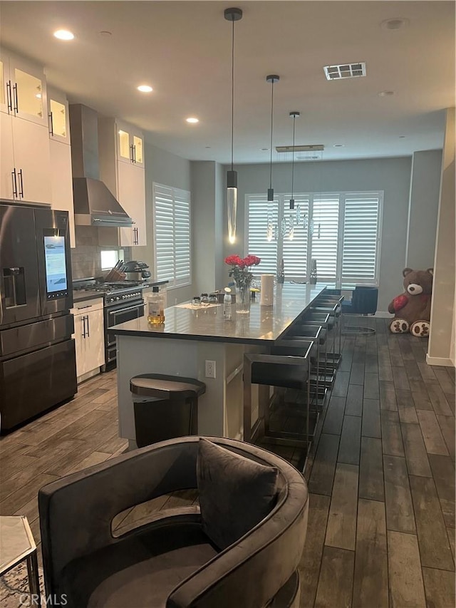 kitchen with pendant lighting, dark wood-type flooring, black refrigerator with ice dispenser, white cabinets, and wall chimney range hood