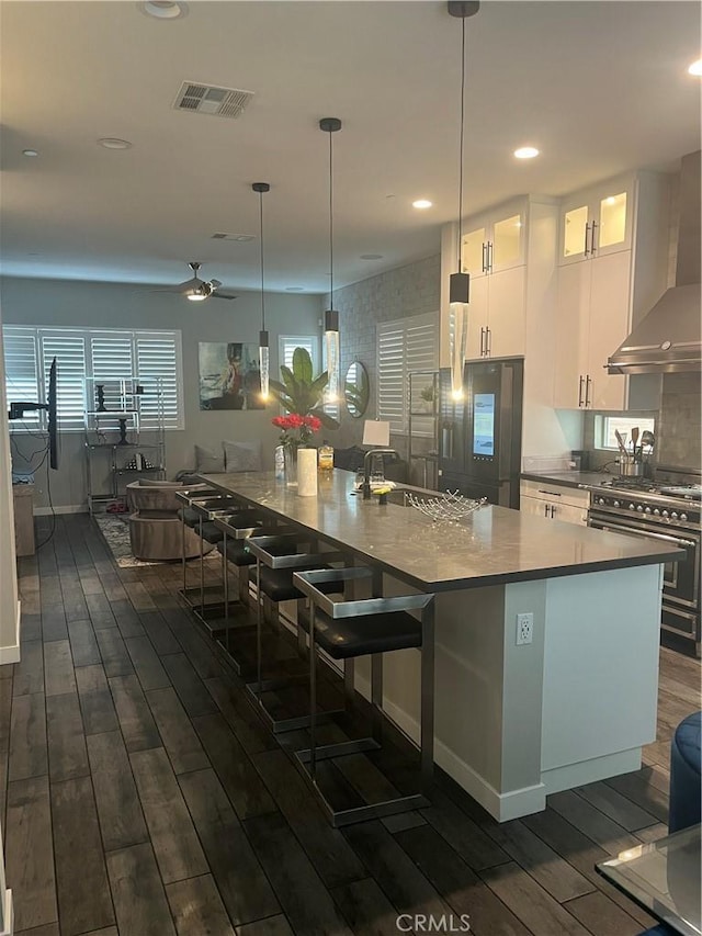 kitchen with double oven range, wall chimney range hood, ceiling fan, dark hardwood / wood-style flooring, and white cabinetry