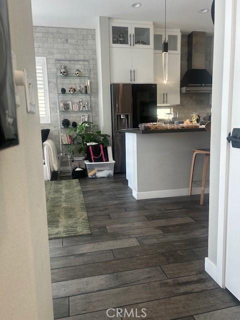 kitchen featuring wall chimney exhaust hood, black fridge, dark hardwood / wood-style flooring, backsplash, and white cabinets