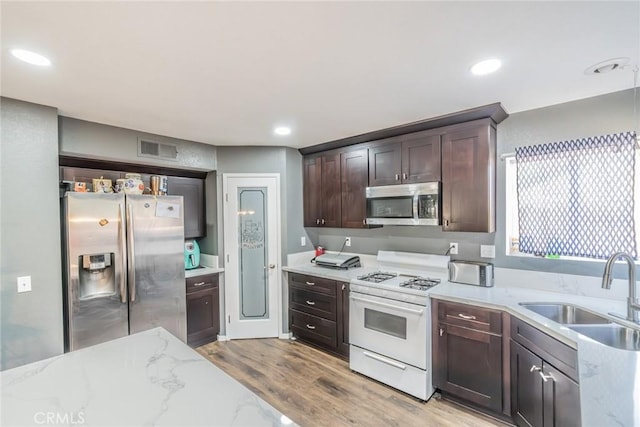 kitchen with sink, stainless steel appliances, light stone counters, light hardwood / wood-style flooring, and dark brown cabinets