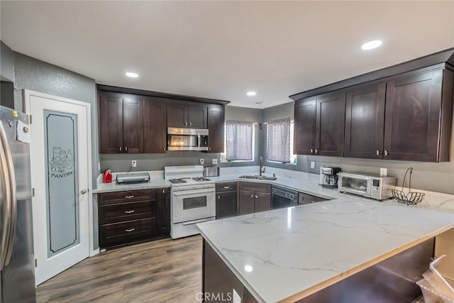 kitchen with kitchen peninsula, sink, appliances with stainless steel finishes, light stone counters, and wood-type flooring