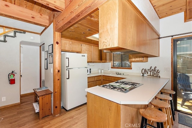 kitchen with kitchen peninsula, light hardwood / wood-style floors, stainless steel gas stovetop, beam ceiling, and white refrigerator