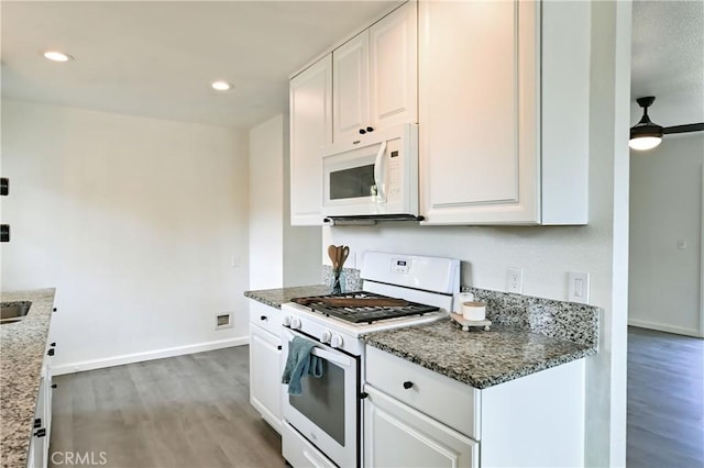 kitchen with dark stone countertops, white cabinetry, wood-type flooring, and white appliances