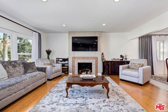 living room with a wealth of natural light, a tiled fireplace, and hardwood / wood-style flooring