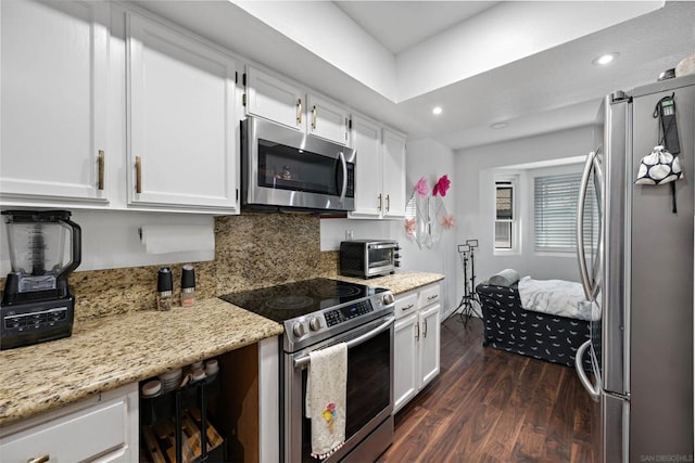 kitchen with decorative backsplash, stainless steel appliances, white cabinets, light stone counters, and dark hardwood / wood-style flooring