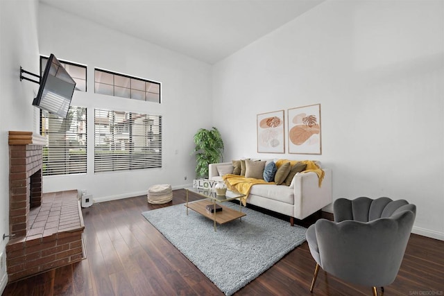 living room featuring a brick fireplace, dark hardwood / wood-style flooring, and a towering ceiling