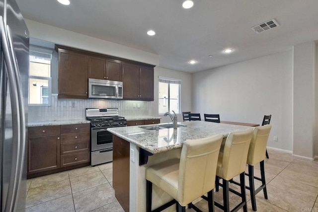 kitchen with a center island with sink, appliances with stainless steel finishes, light stone countertops, a kitchen bar, and sink