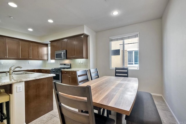 kitchen with light stone countertops, sink, backsplash, stainless steel appliances, and light tile patterned floors