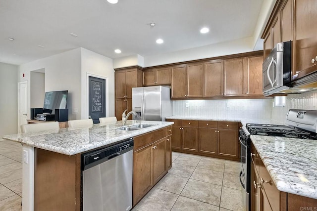 kitchen with a center island with sink, sink, light tile patterned floors, appliances with stainless steel finishes, and light stone counters